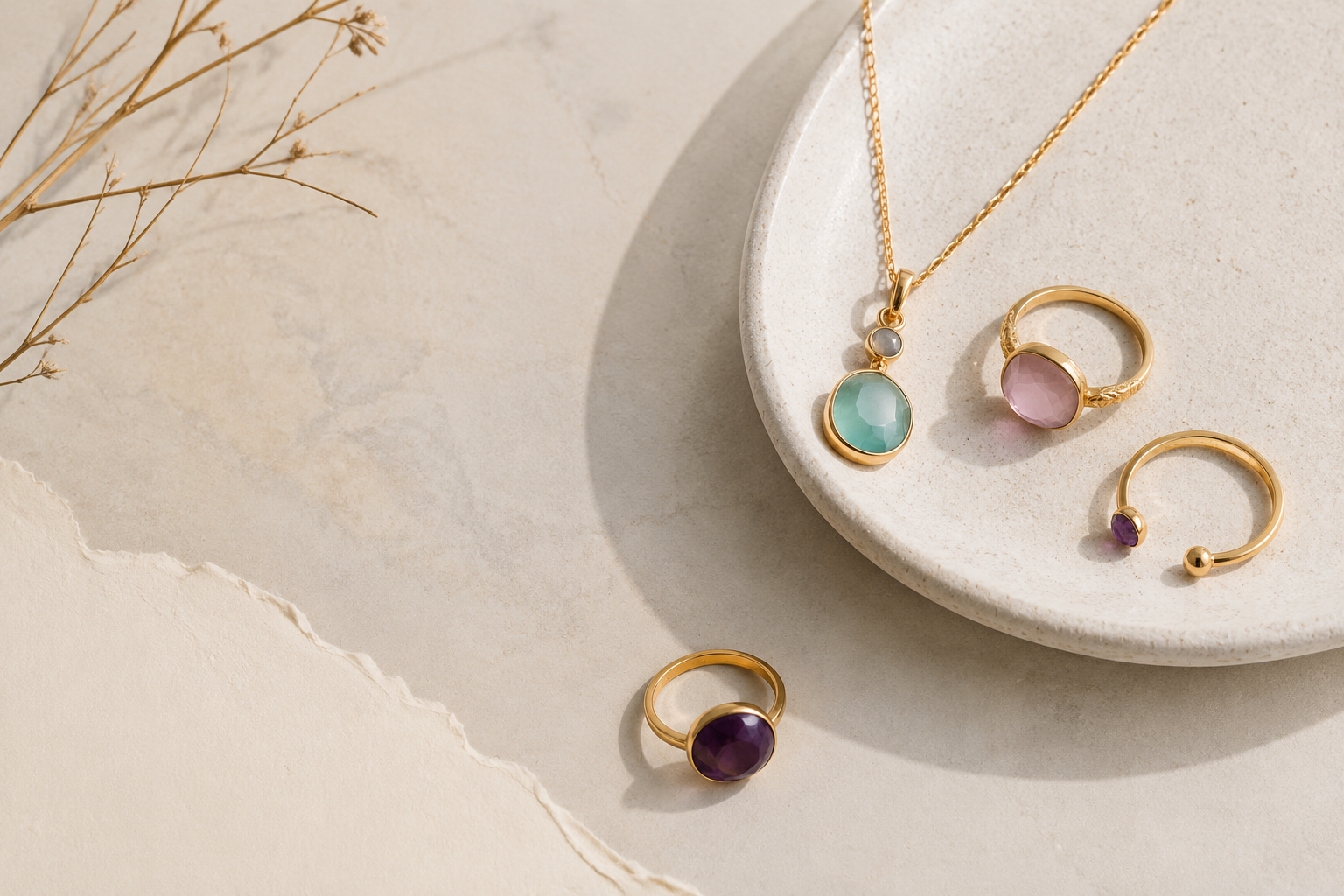 Minimalist flat-lay featuring gold jewelry with semiprecious stones, including a green pendant necklace and two gemstone rings, set on a beige textured surface.