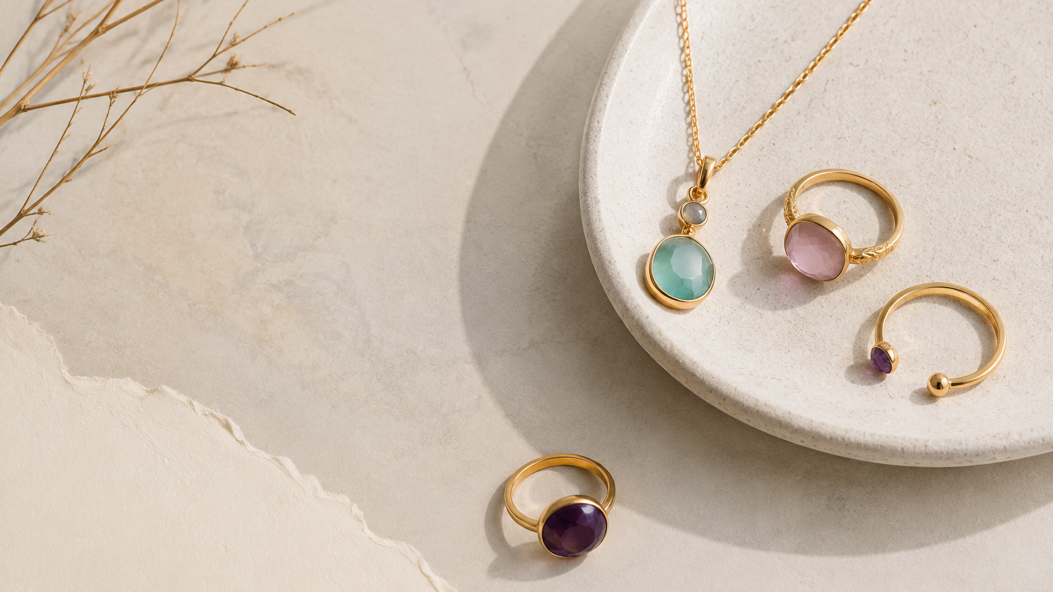 Minimalist flat-lay featuring gold jewelry with semiprecious stones, including a green pendant necklace and two gemstone rings, set on a beige textured surface.