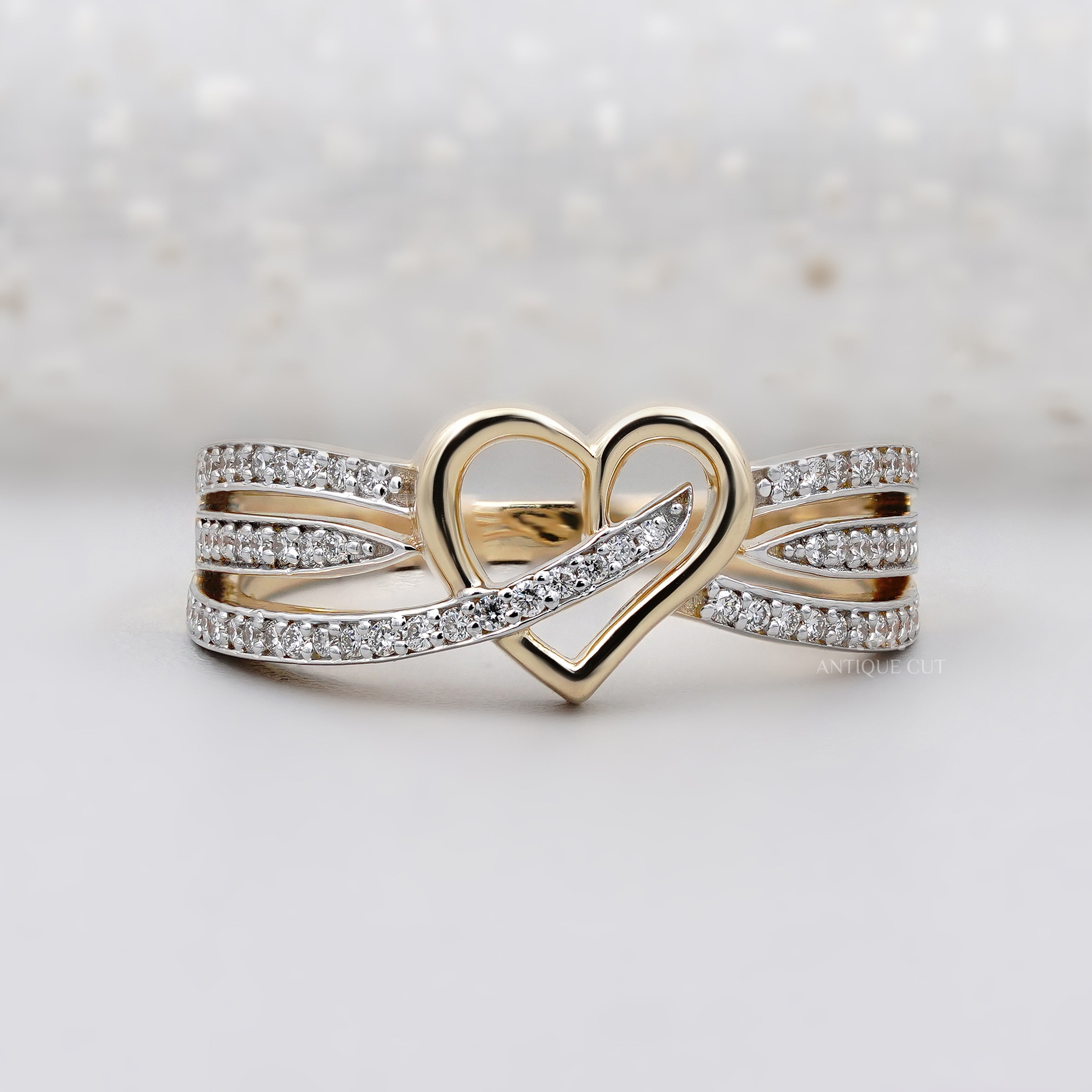 Gold heart-shaped ring with diamond accents on a light background

