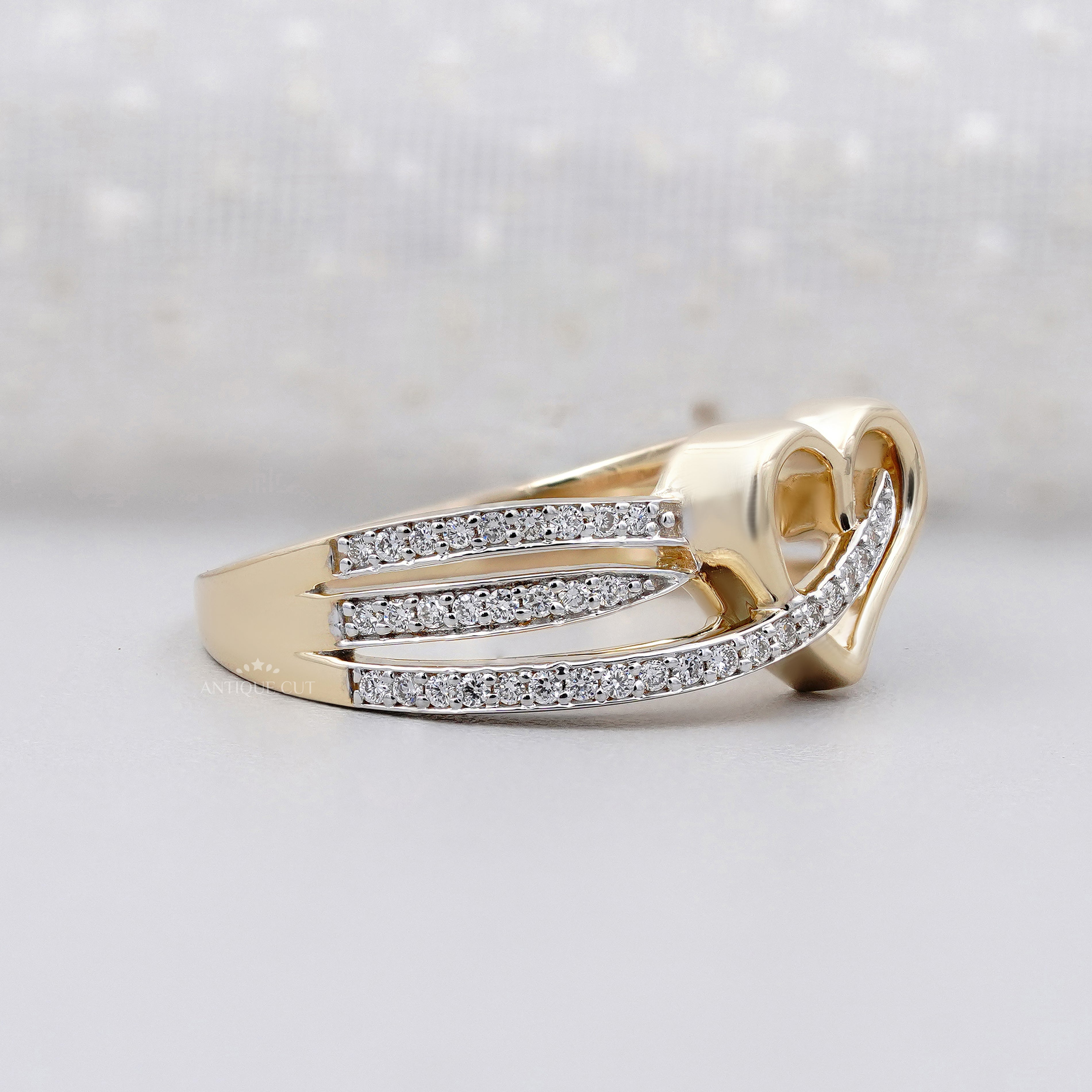 Gold heart-shaped ring with diamond accents on a light background

