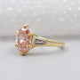Gold ring with a pink diamond and baguette cut diamonds on a light background