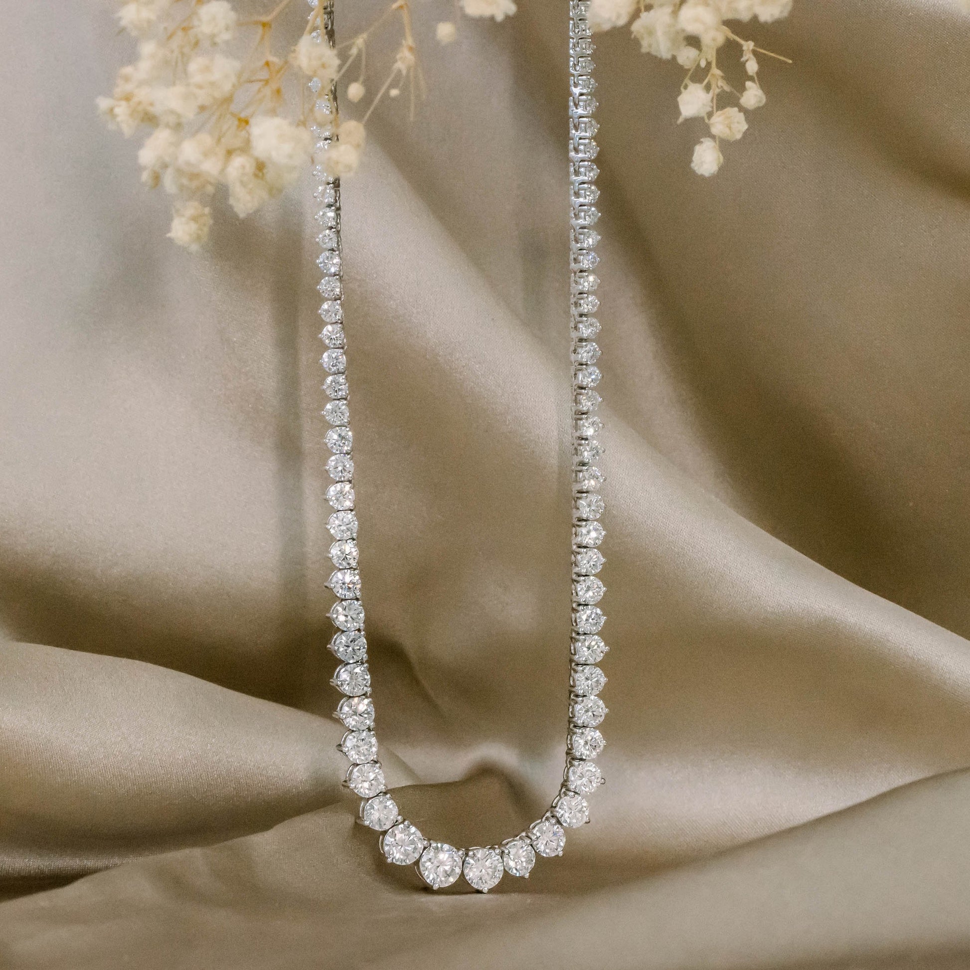 Diamond tennis necklace on satin fabric with flowers.
