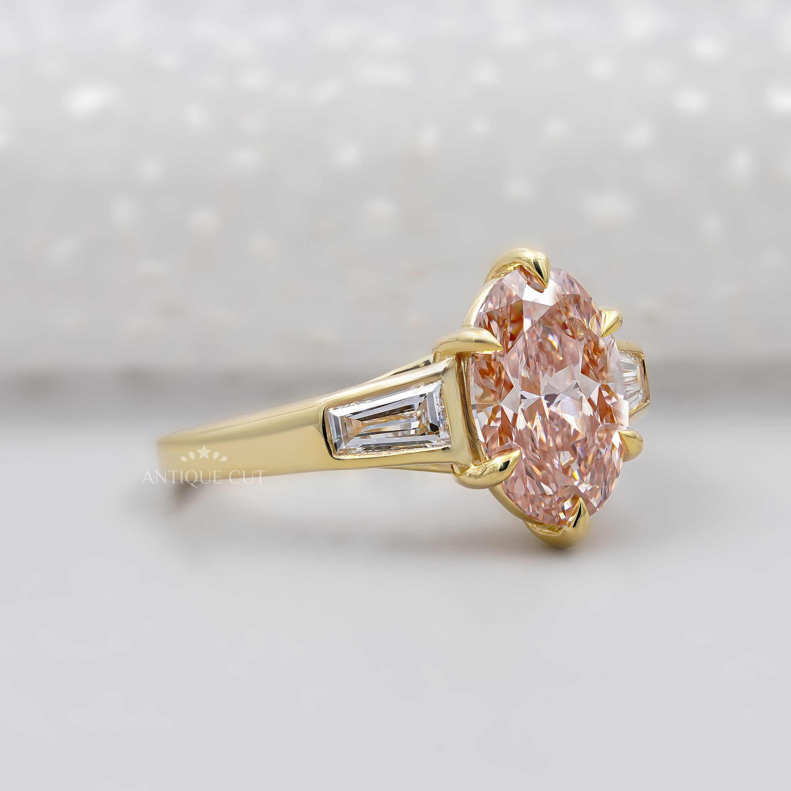 Gold ring with a pink diamond and baguette cut diamonds on a light background