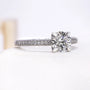 Round center diamond held by four prongs above a pavé band
