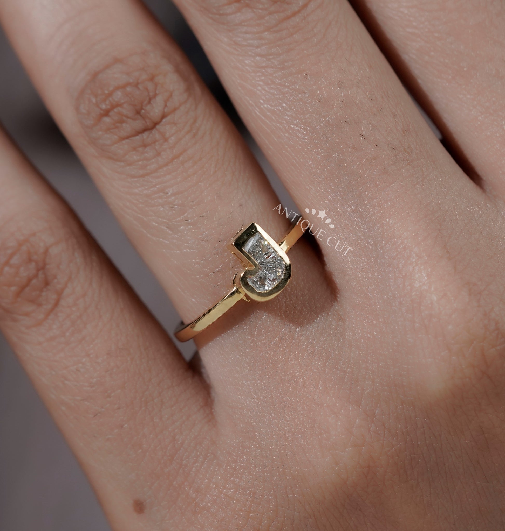 Yellow gold J letter engagement ring featuring a bezel set lab grown diamond