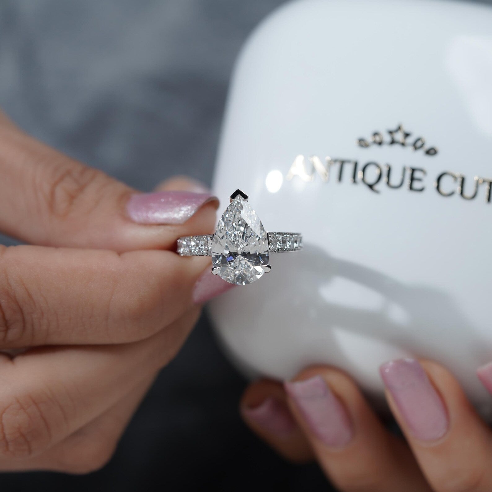 Diamond ring held by a hand with a blurred 'Antiquecut' background


