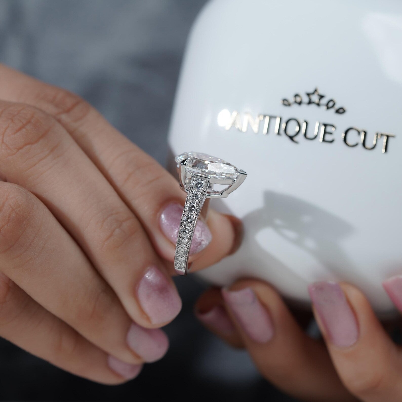 Diamond ring held by a hand with a 'Vintage Cut' branded box in the background

