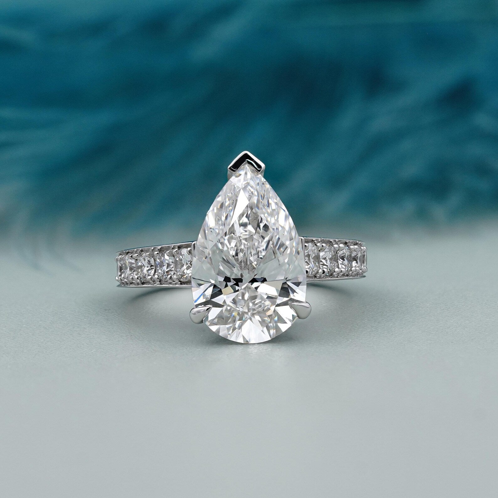 Diamond ring with a pear-shaped center stone on a light gray background

