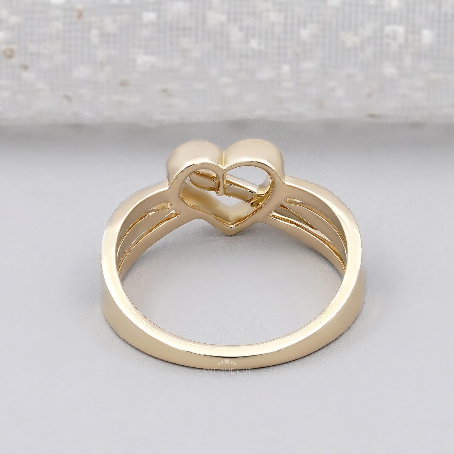 Gold ring with a heart and infinity symbol on a light gray background


