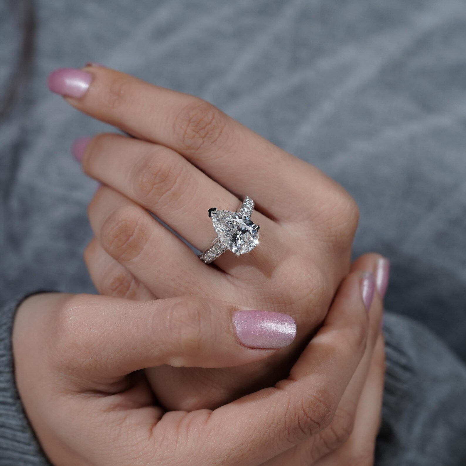 Close-up of a hand wearing a diamond ring with a blurred gray background

