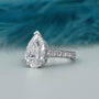 Diamond ring with pear-shaped center stone and smaller stones on band against a blurred blue and gray background

