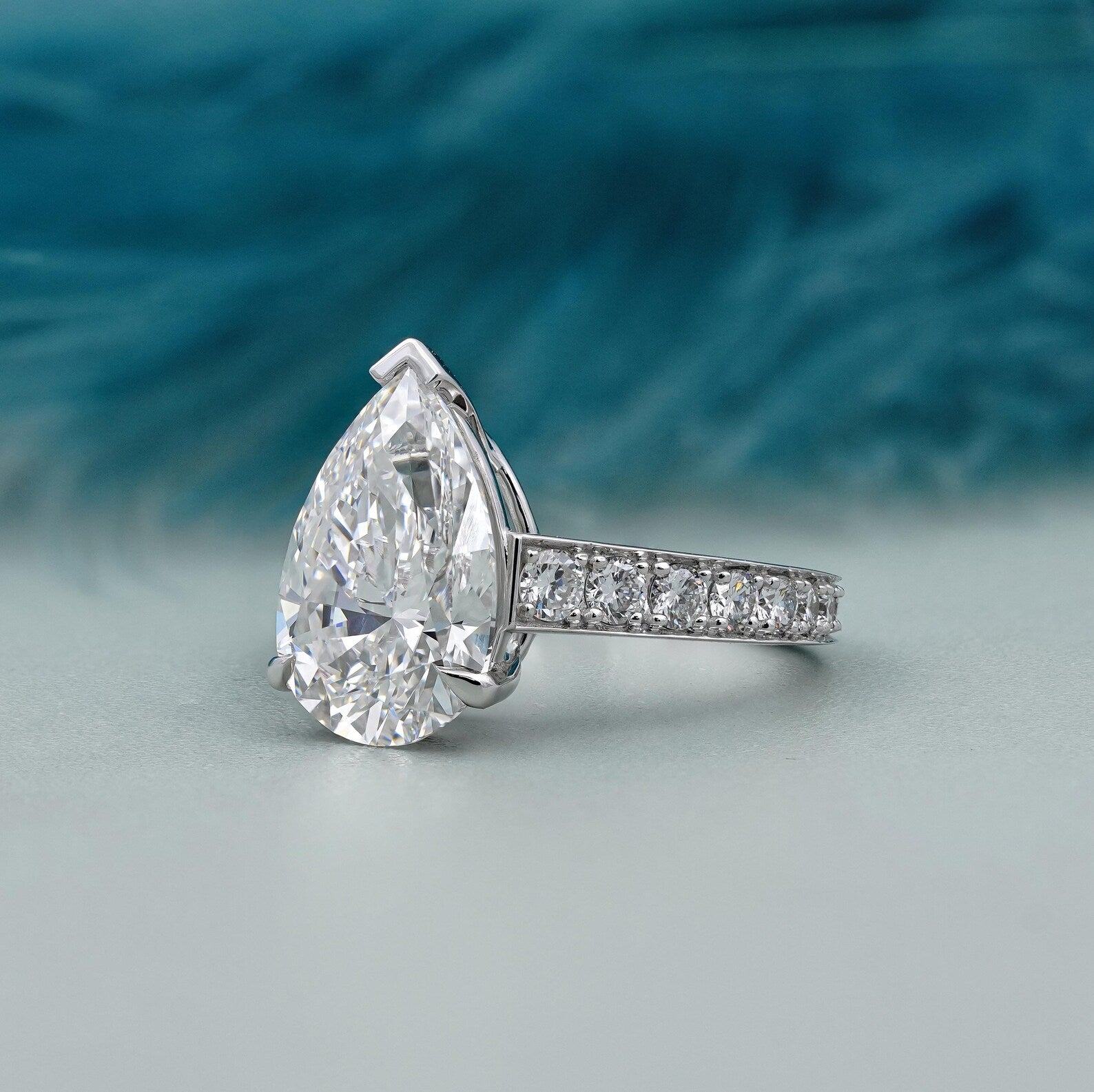 Diamond ring with pear-shaped center stone and smaller stones on band against a blurred blue and gray background

