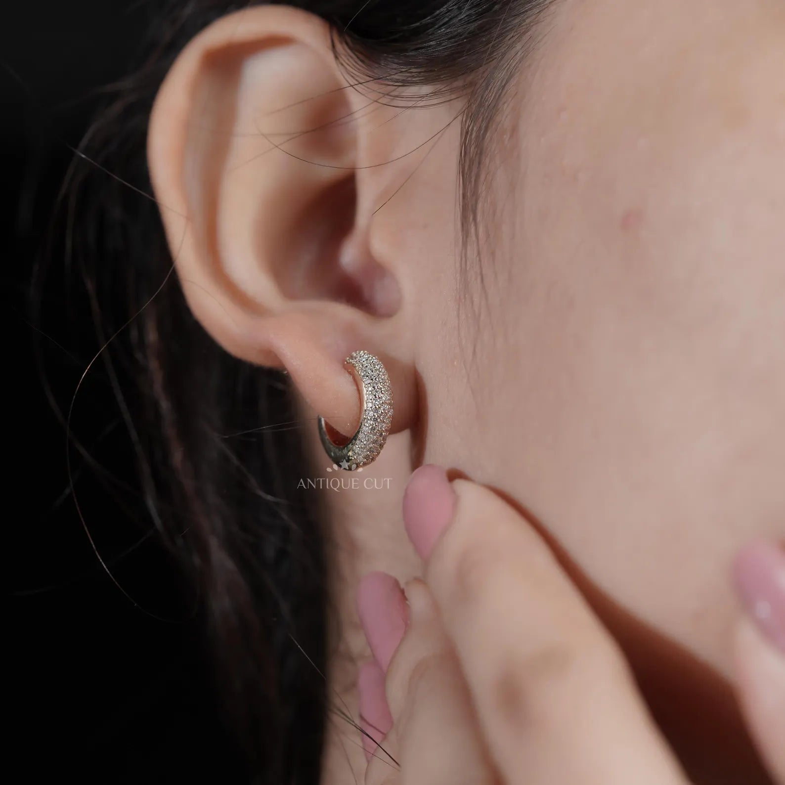 Close-up of an ear wearing a silver earring with a hand adjusting it.

