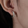 Close-up of an ear wearing a silver earring with a hand adjusting it.

