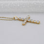 Gold cross necklace with clear stones on a gray background