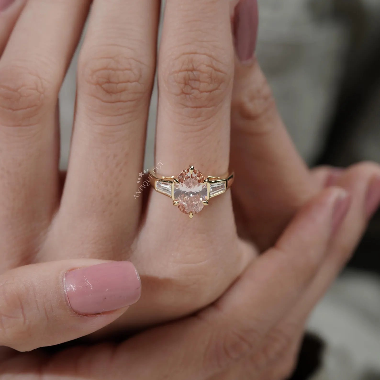 Close-up of a hand wearing a rose gold ring with a pink gemstone.
