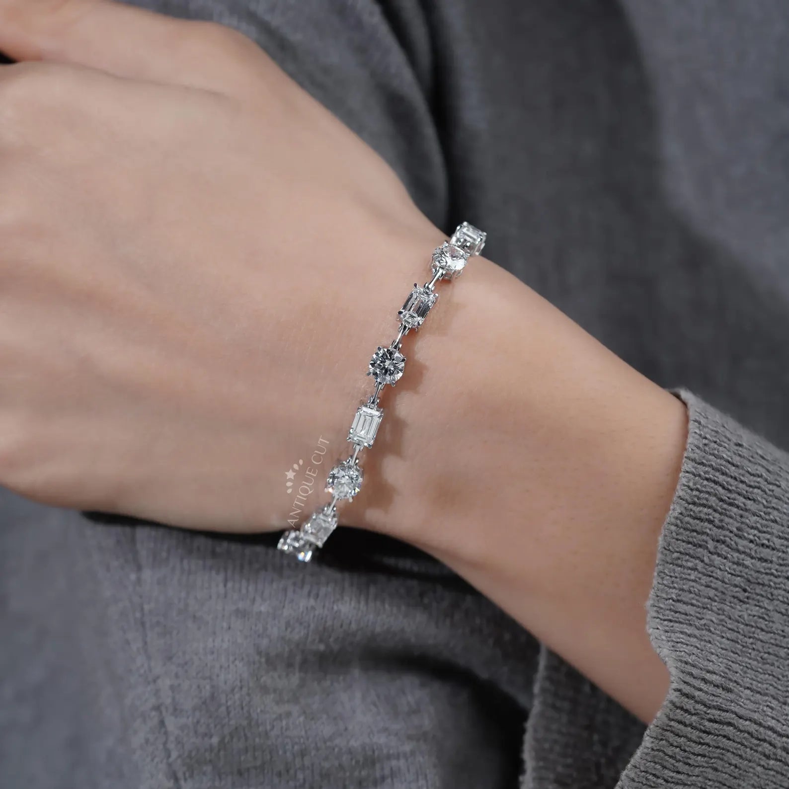 Silver bracelet with clear stones on a wrist against a gray background