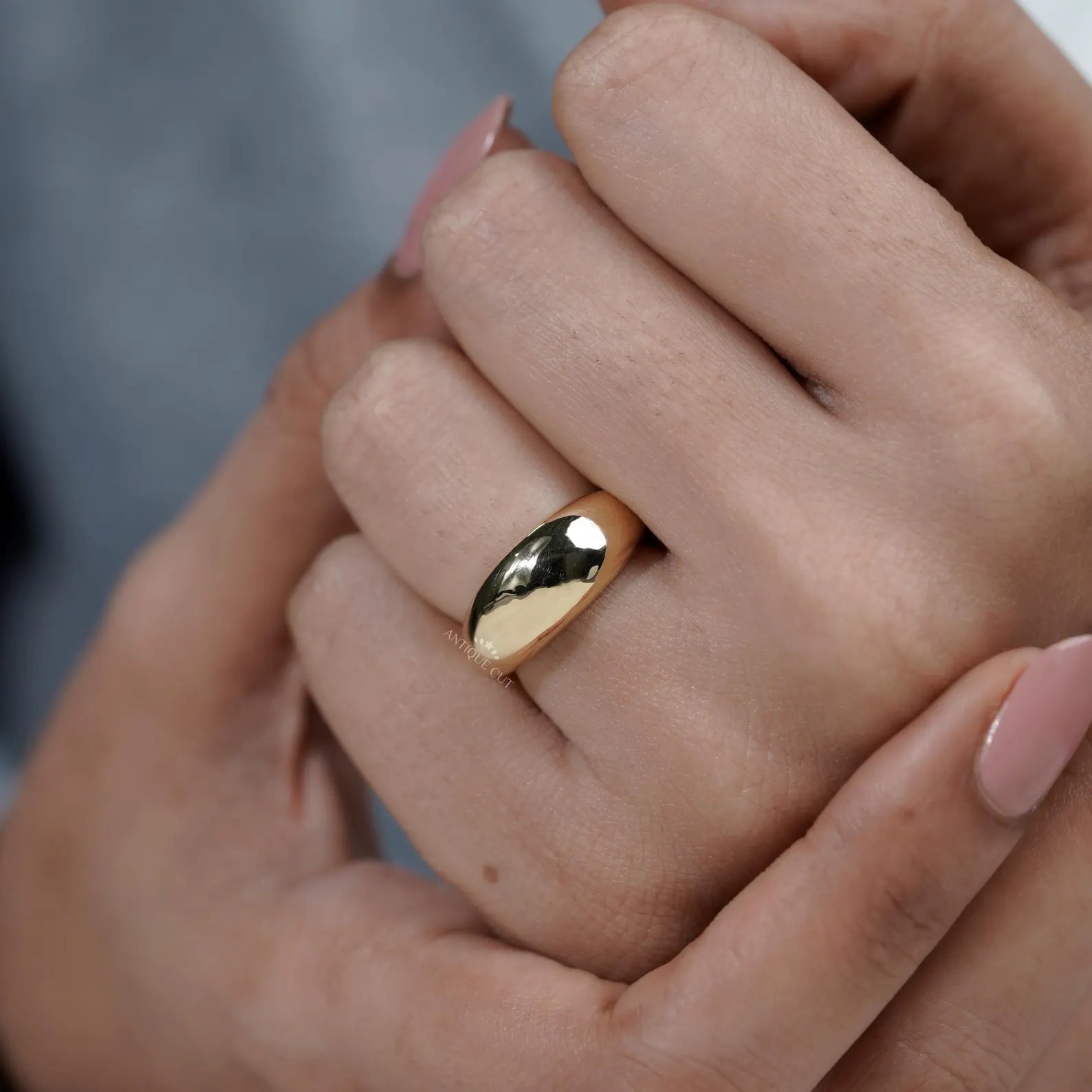 Close-up of a hand wearing a gold ring with a blurred background

