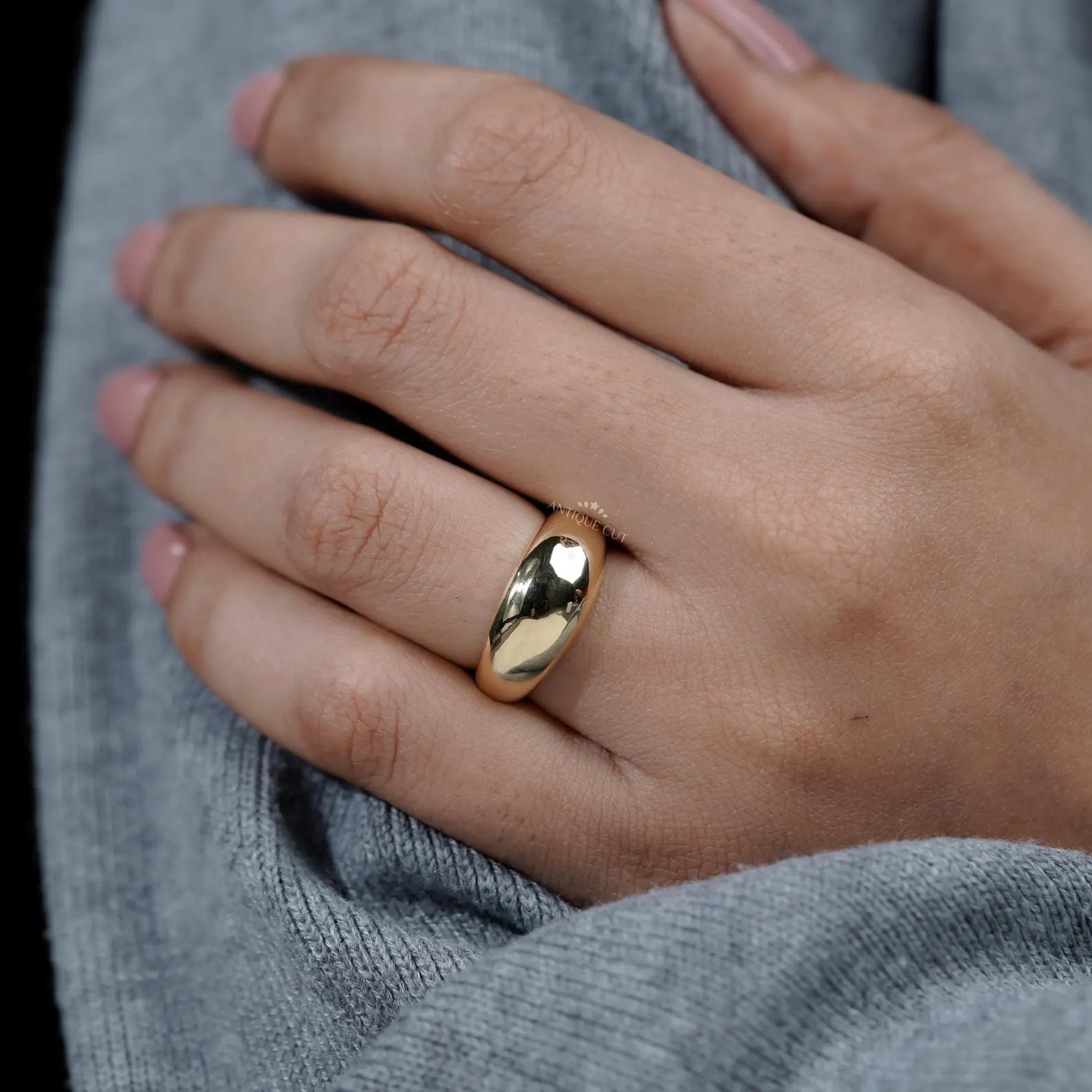 Close-up of a hand wearing a gold ring with a blurred background

