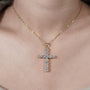 Gold cross necklace with clear stones on a gray background