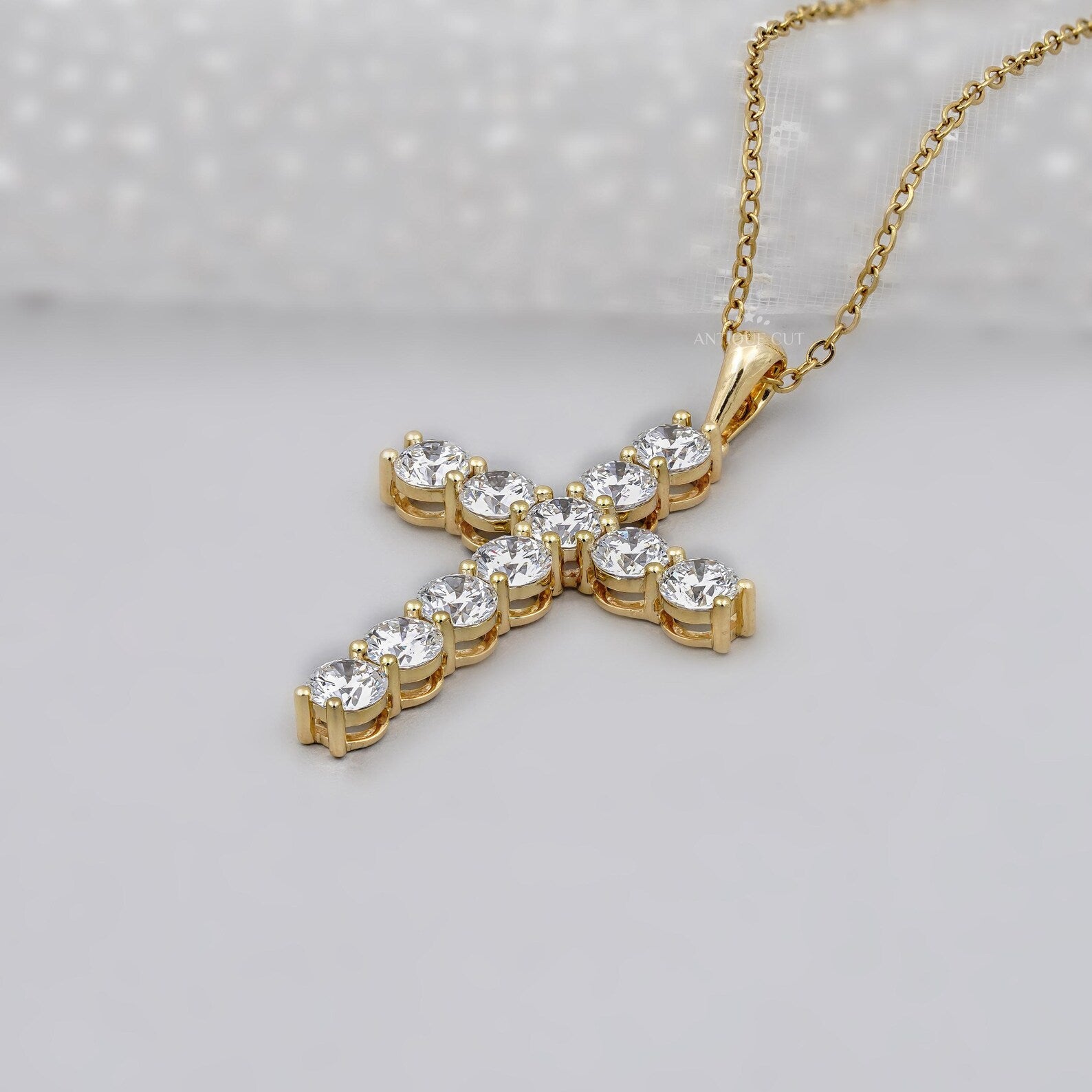 Gold cross necklace with clear stones on a gray background