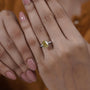 Close-up of a hand wearing a yellow diamond ring with a blurred background

