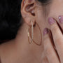 Gold hoop earrings held by a hand with a blurred 'Antique Cut' container in the background.