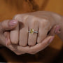 Close-up of a hand wearing a yellow diamond ring with a blurred background