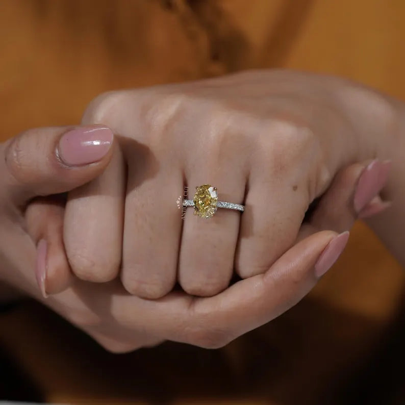 Close-up of a hand wearing a yellow diamond ring with a blurred background