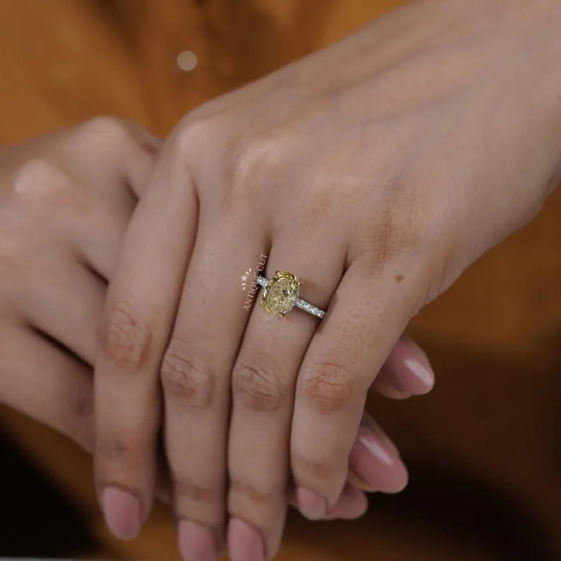 Close-up of a hand wearing a yellow diamond ring on a blurred background