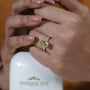 Close-up of a hand wearing a yellow gemstone ring with 'Antiquecut' branding in the background.