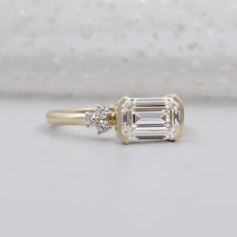 East west emerald diamond ring with sleek half bezel yellow gold band