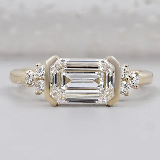 East west emerald cut diamond ring in yellow gold half bezel setting