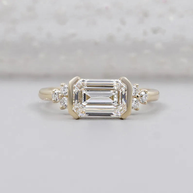 East west emerald cut diamond ring in yellow gold half bezel setting