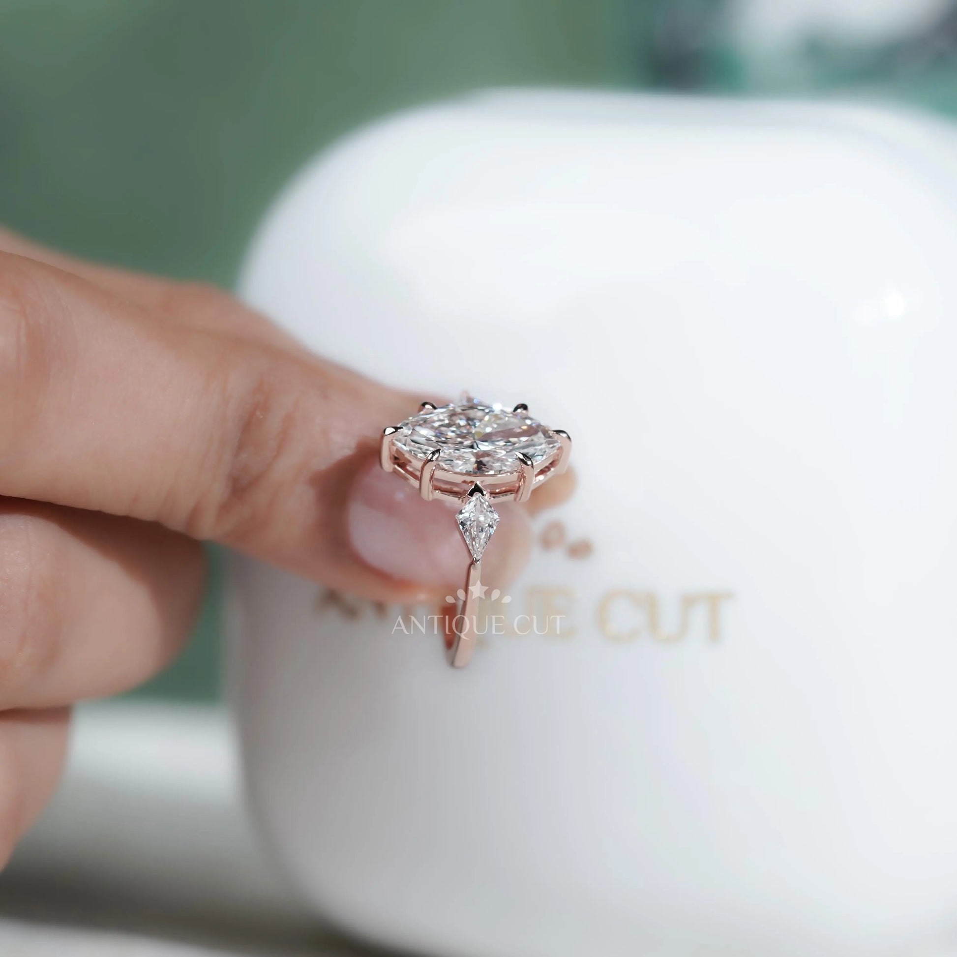 Diamond ring held by a hand with 'AntiqueCut' branding in the background