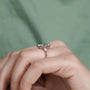 Rose gold ring with a diamond on a hand against a green background

