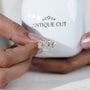 Diamond ring held by a hand in front of an 'Antiquecut' branded box.