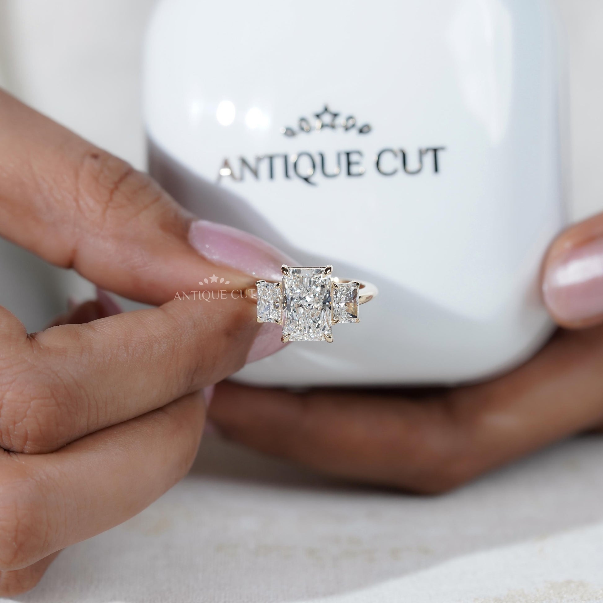 Diamond ring held by a hand in front of an 'Antiquecut' branded box.