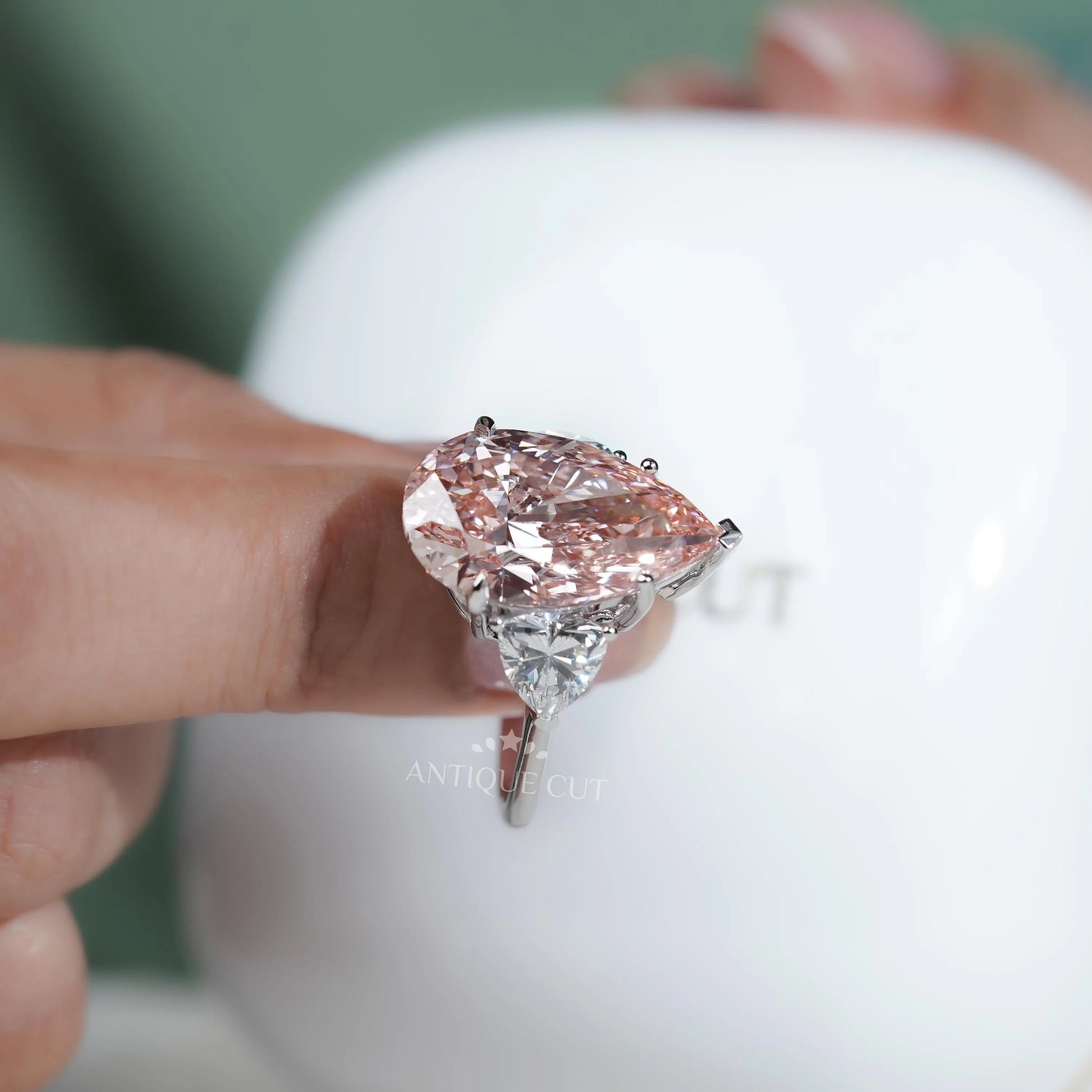 Teardrop-shaped pink diamond held between fingers with a blurred background

