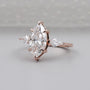 Rose gold ring with a large pear-shaped diamond and smaller diamonds on a light gray background

