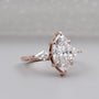 Rose gold ring with a large marquise-shaped diamond and smaller side stones on a light gray background.

