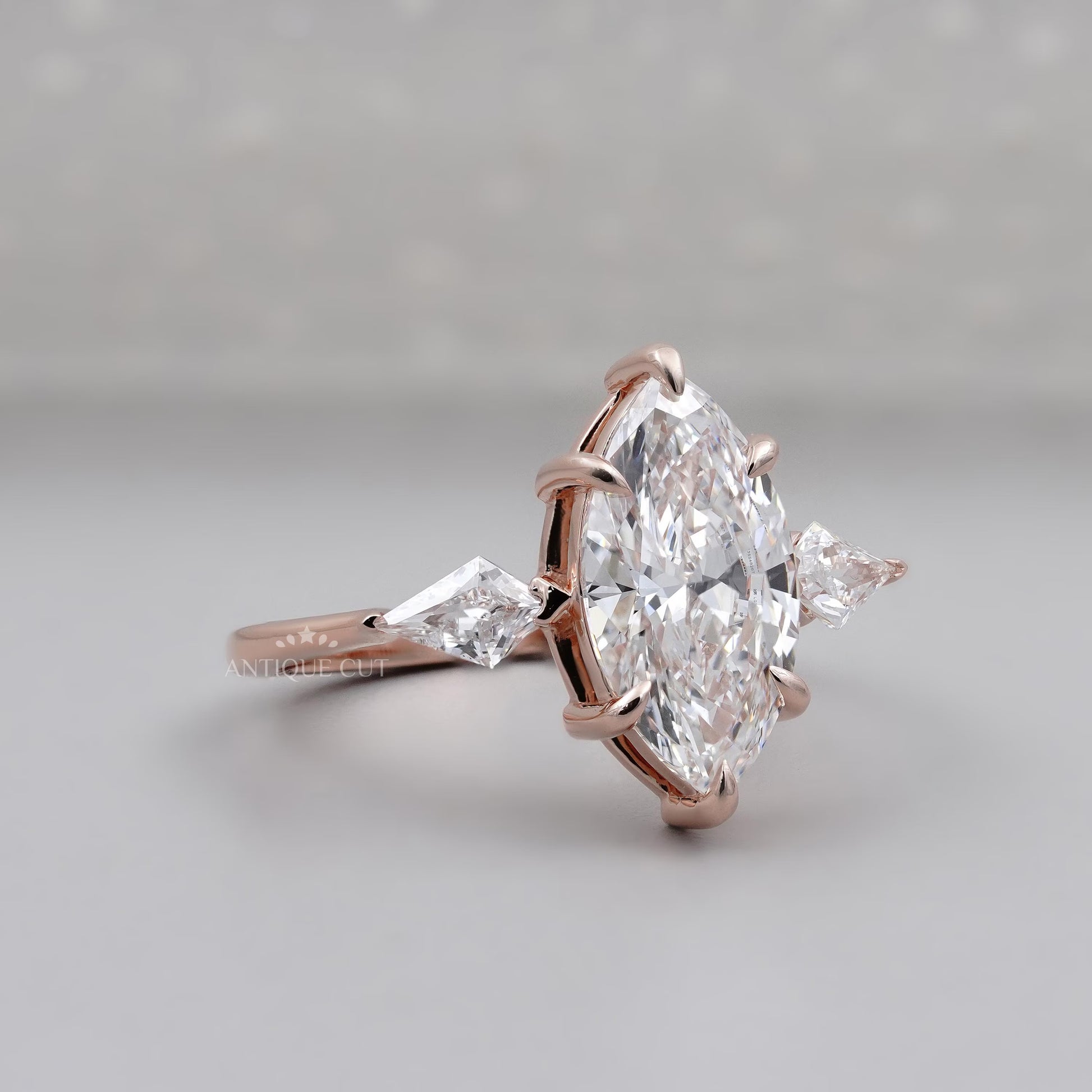 Rose gold ring with a large marquise-shaped diamond and smaller side stones on a light gray background.

