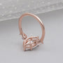 Rose gold ring with a large central gemstone and smaller stones on a light gray background

