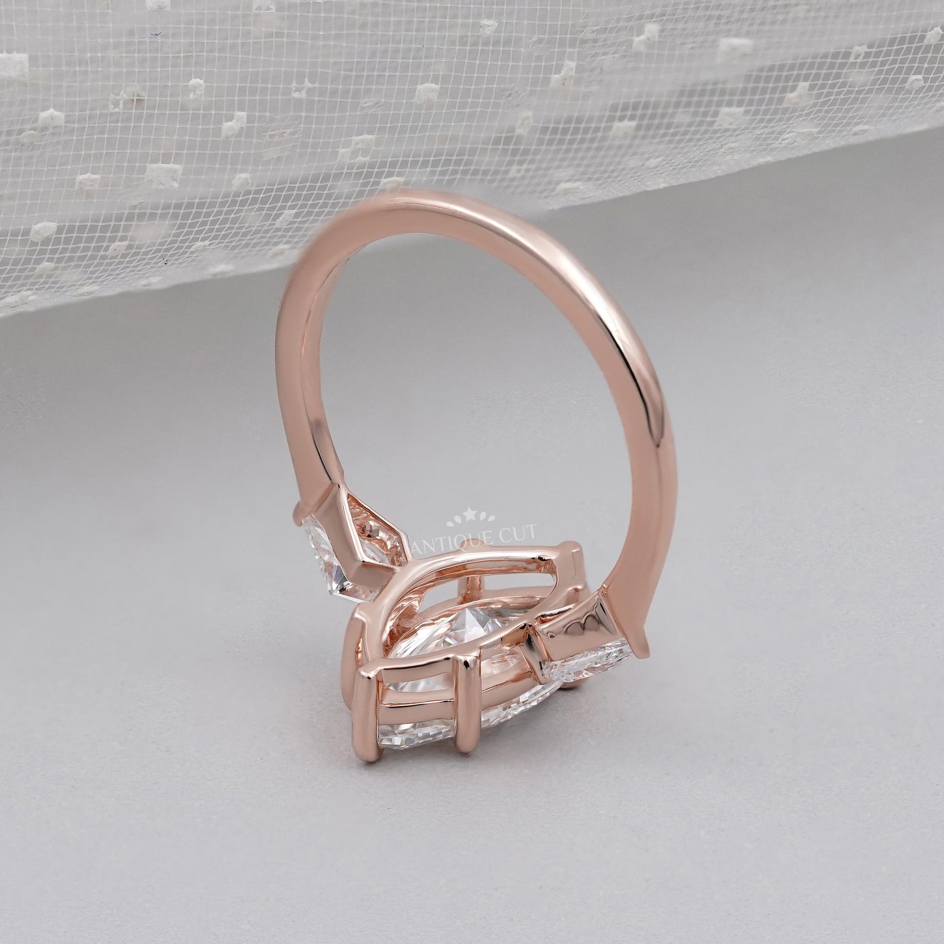 Rose gold ring with a large central gemstone and smaller stones on a light gray background

