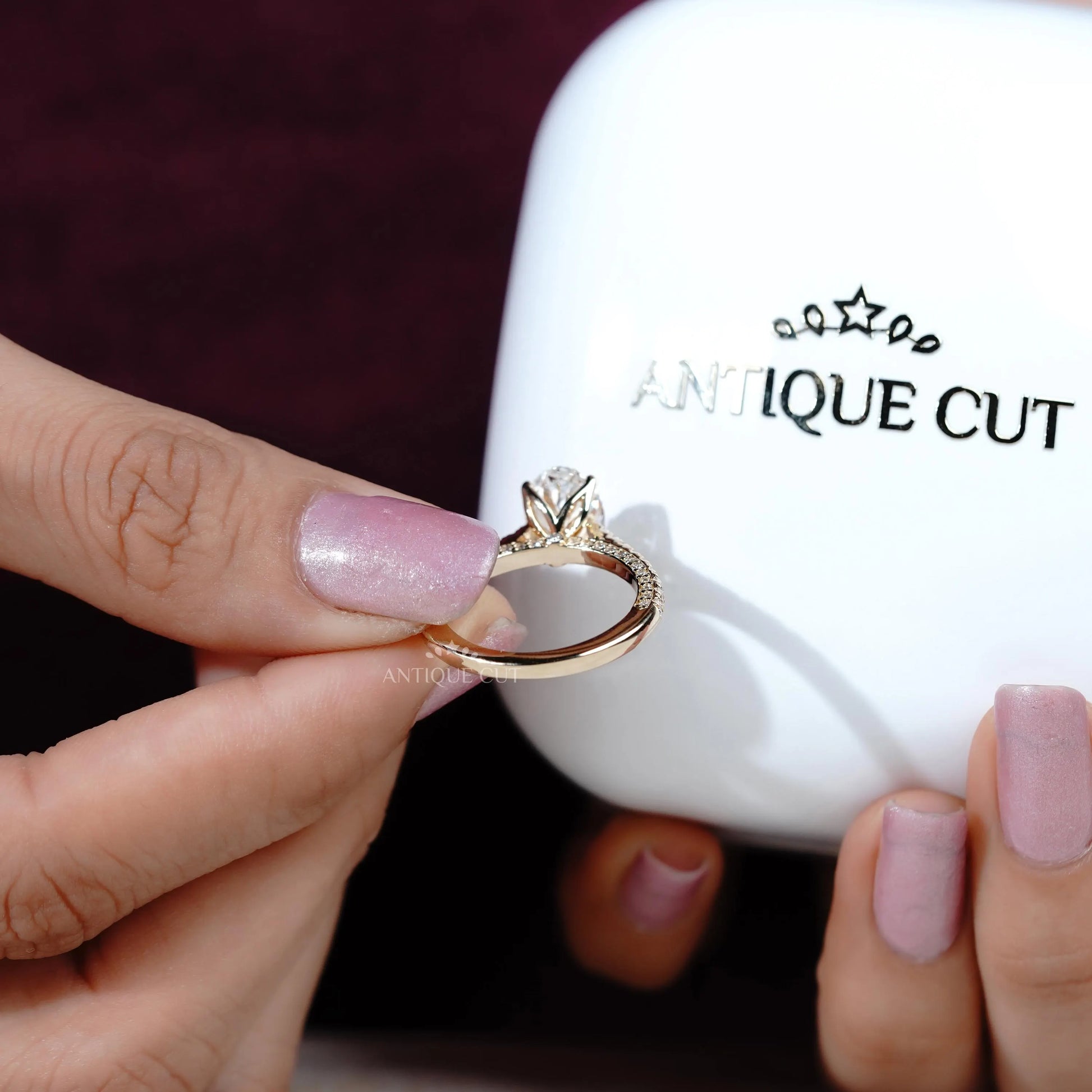 Hand holding a diamond ring with 'Antiquecut' branding in the background