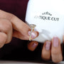 Hand holding a diamond ring with 'Antiquecut' branding in the background