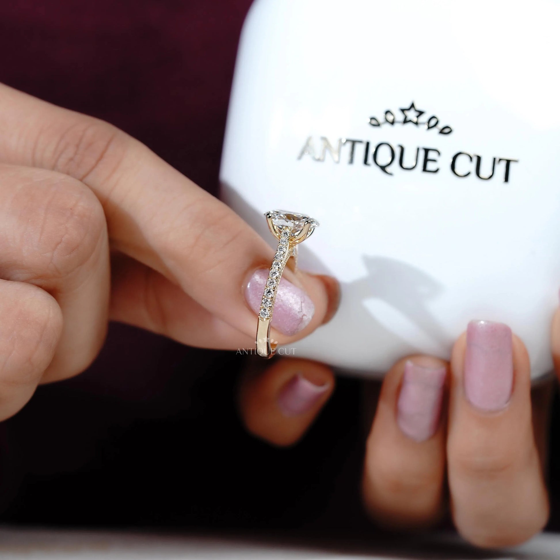 Hand holding a diamond ring with 'Antiquecut' branding in the background