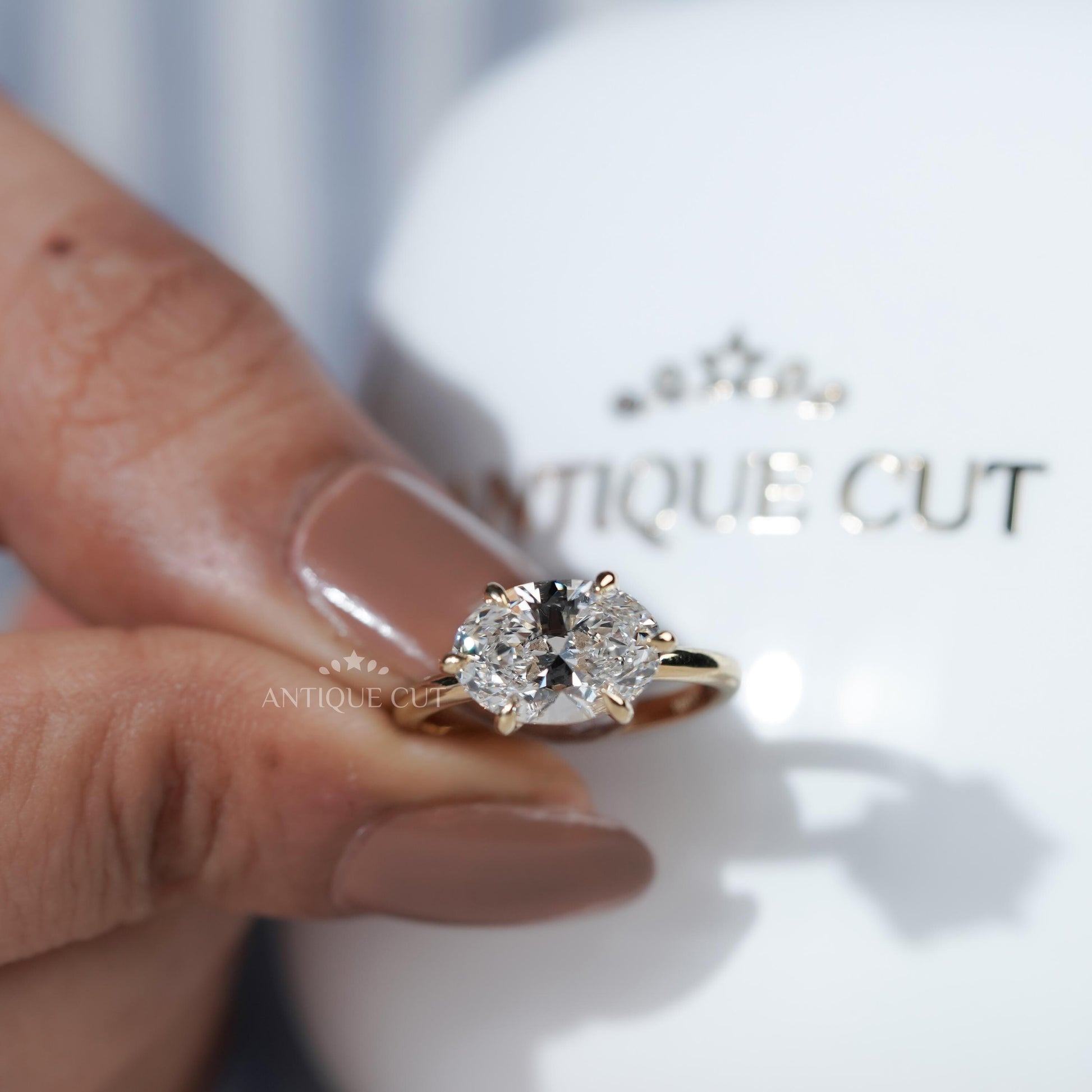 Gold ring with two diamonds held by a hand on a Antiquecut branded background