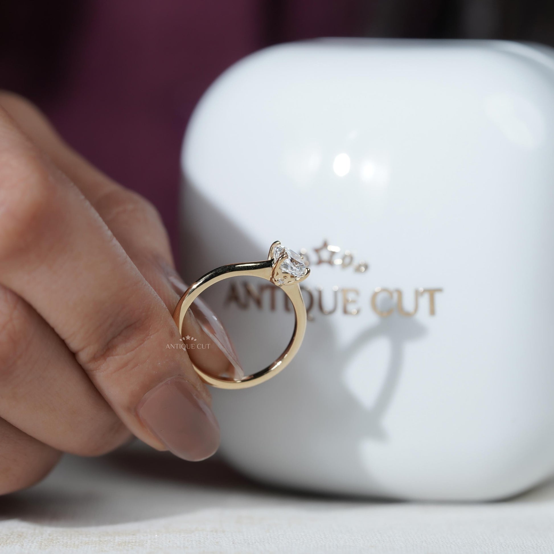 Gold ring with a diamond held by a hand in front of a white container 