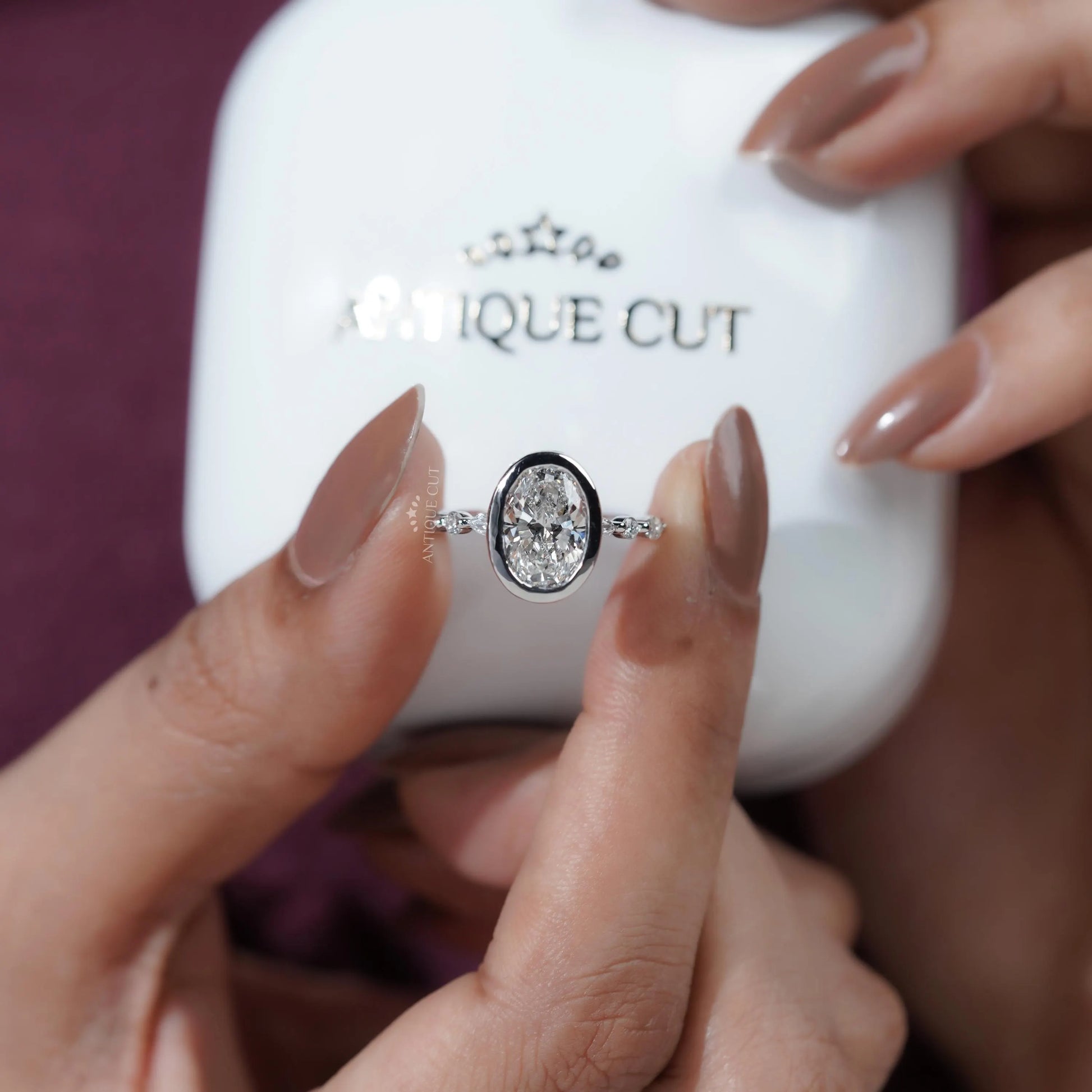 Diamond ring held by a hand in front of a white box